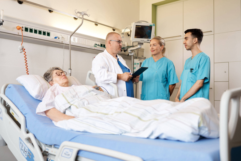 Ein Arzt und zwei Pflegekräfte stehen besprechend am Krankenbett einer liegenden Patientin.