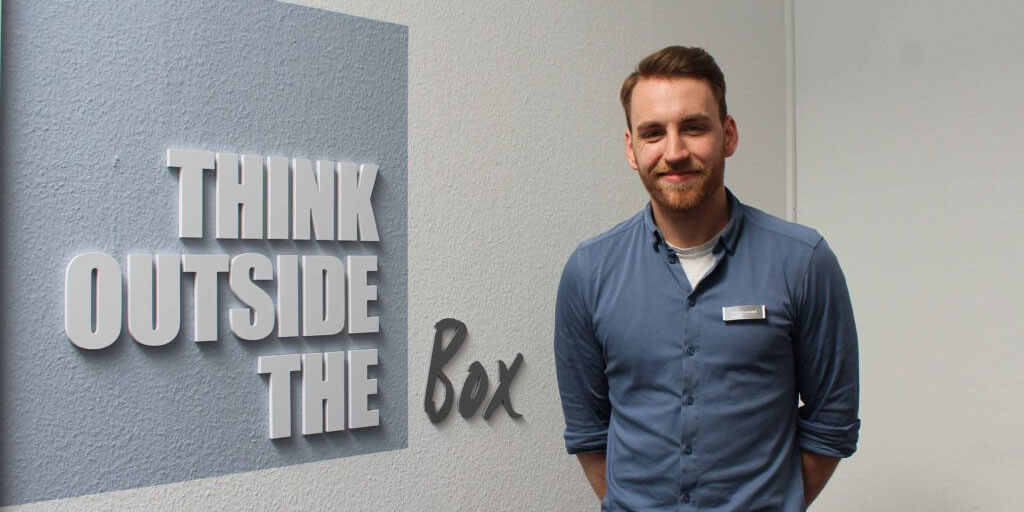 Portraitfoto von Lars Ruelander, lächelnd, neben einem Wandtattoo mit dem Schriftzug "THINK OUTSIDE THE BOX".