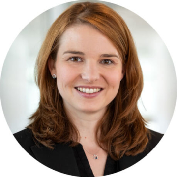 Porträtfoto einer lächelnden Frau mit braunen, schulterlangen Haaren im dunklen Blazer.