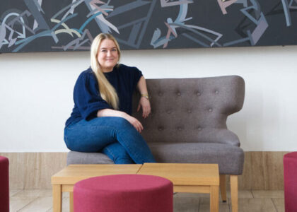 Leonie Ludewig sitzt lächelnd auf einem grauen Sofa vor einer Wand mit moderner Kunst.