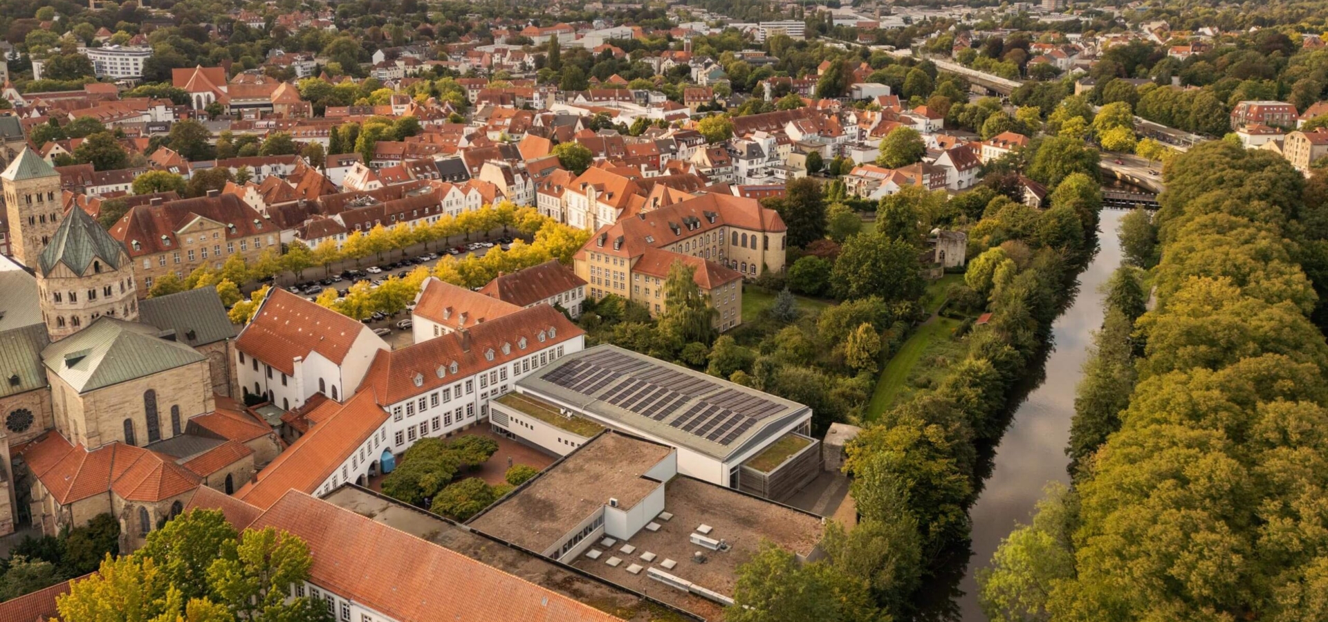 Vogelperspektive auf eine historische Stadt mit rotdachigen Gebäuden, einem Dom, vielen Bäumen und einem Flusslauf.