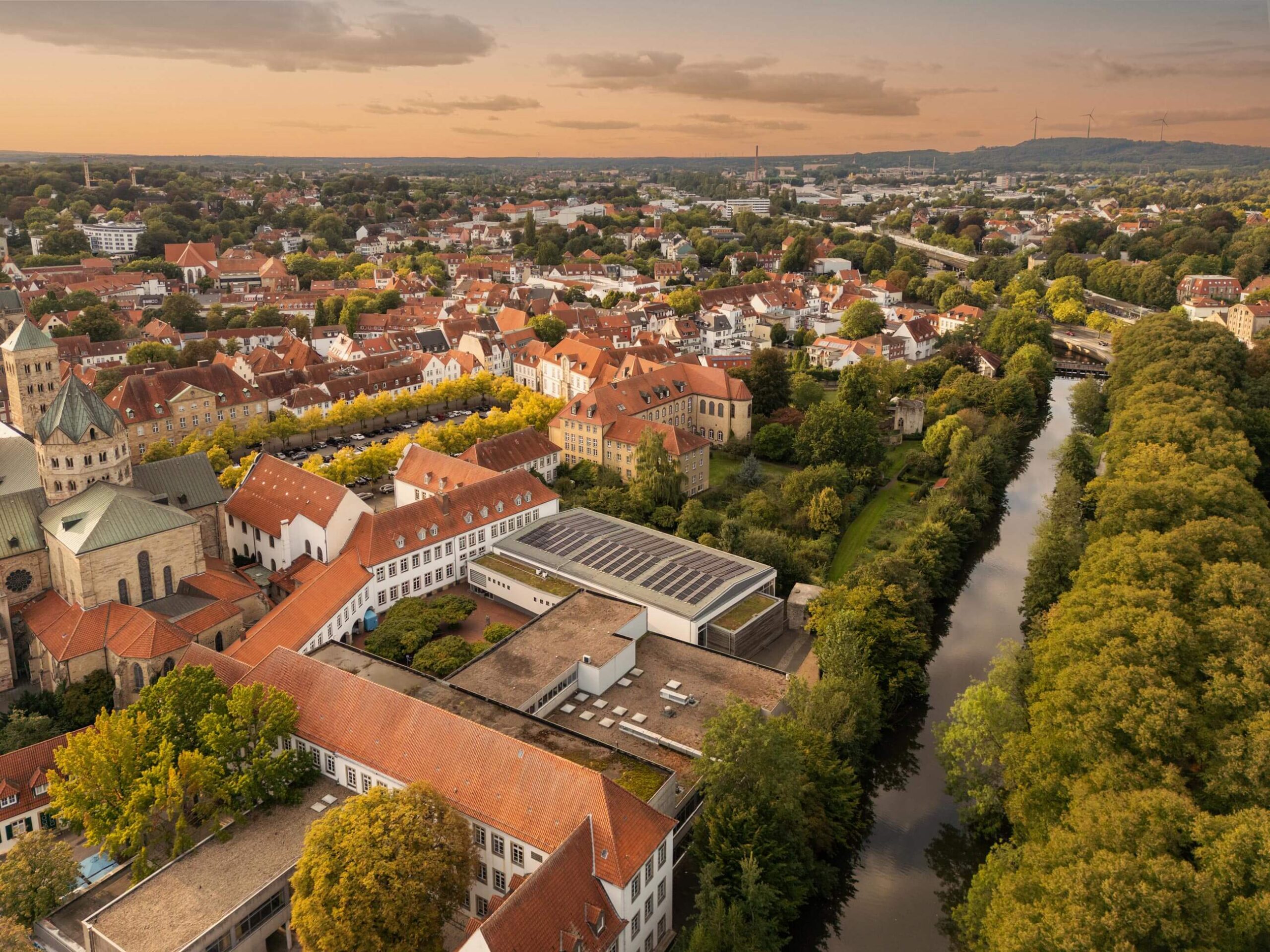 Vogelperspektive auf eine historische Stadt mit rotdachigen Gebäuden, einem Dom, vielen Bäumen und einem Flusslauf.