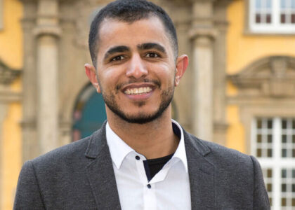 Portrait von Mahmoud Farrag im grauen Sakko und weißen Hemd vor einem historischen, gelben Gebäude.