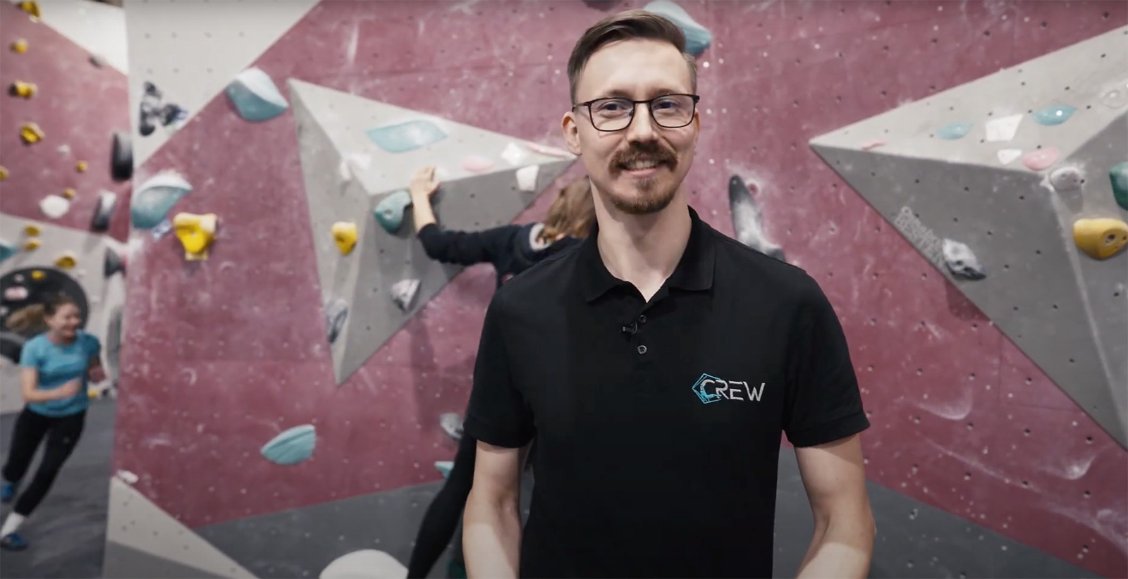 Ein lächelnder Mann mit Brille steht im Vordergrund einer Boulderdach-Halle.