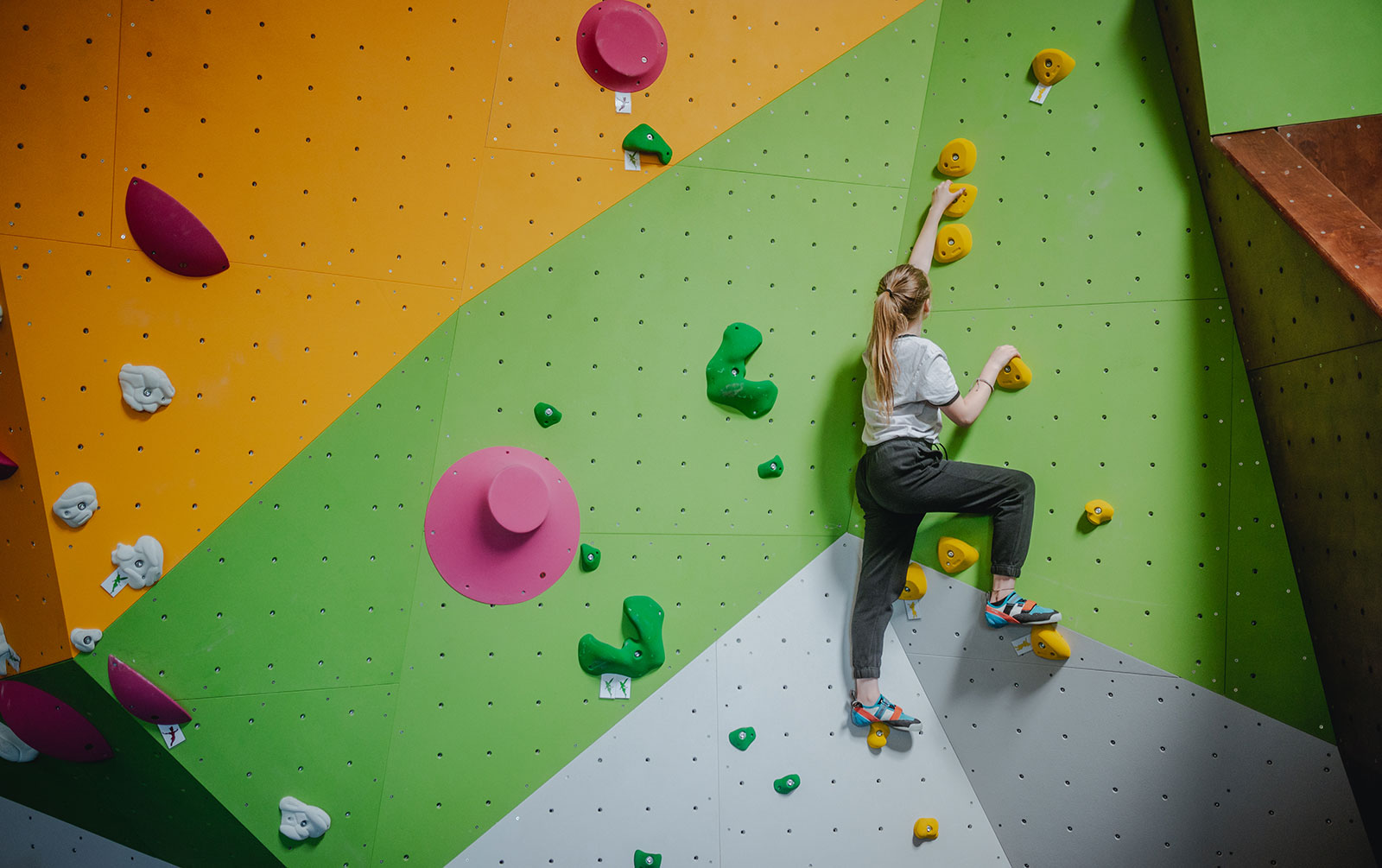Ein Mädchen klettert an einer bunt gestalteten Kletterwand in einer Boulderdach-Halle.