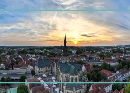 Panorama der Stadt Osnabrück bei Sonnenuntergang mit historischer Marienkirche und dem Rathaus im Zentrum unter leicht bewölktem Abendhimmel.