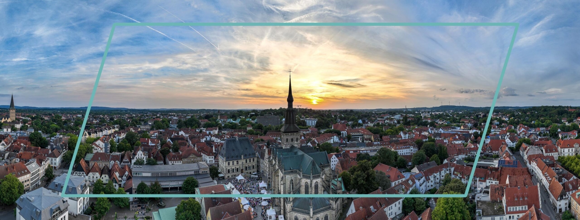 Panorama der Stadt Osnabrück bei Sonnenuntergang mit historischer Marienkirche und dem Rathaus im Zentrum unter leicht bewölktem Abendhimmel.