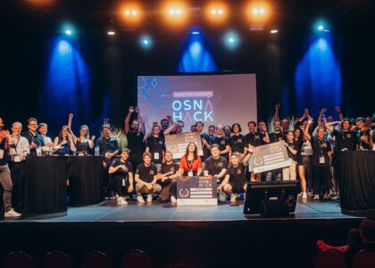 Viele Teilnehmer feiern mit großen Gewinnerschecks auf der beleuchteten Bühne der Hackathon-Veranstaltung OSNA HACK.