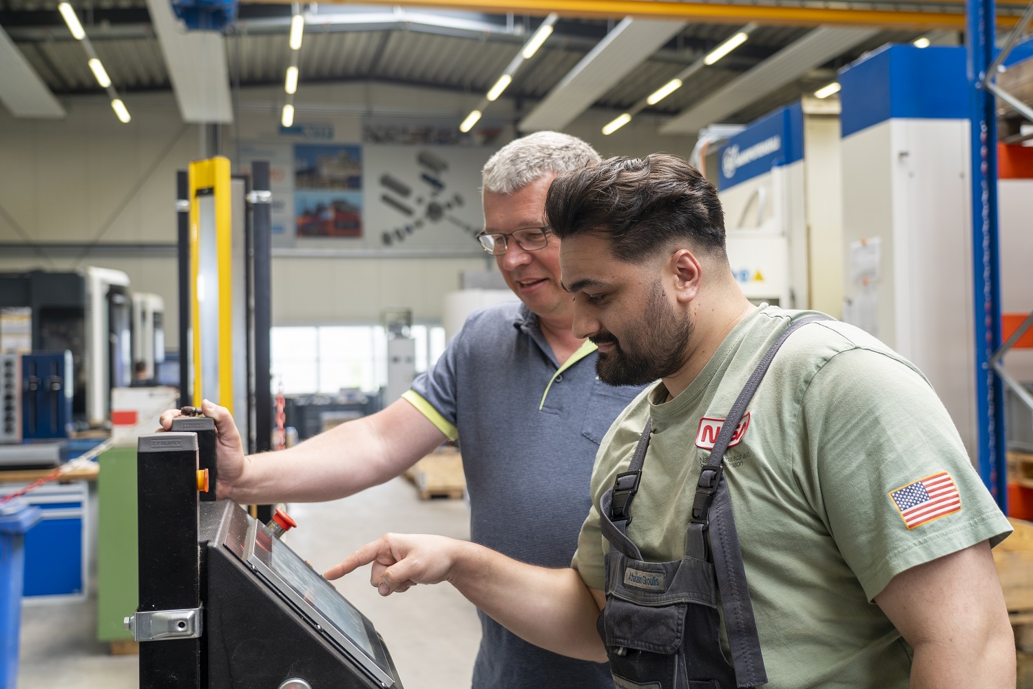 Zwei Männer bedienen gemeinsam ein digitales Steuerungspanel an einer Maschine in einer Produktionshalle.