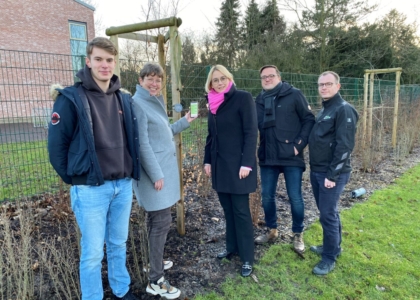 Fünf Personen stehen im Freien vor einem neuen Baum und präsentieren ein Smartphone mit einer grünen Oberfläche.