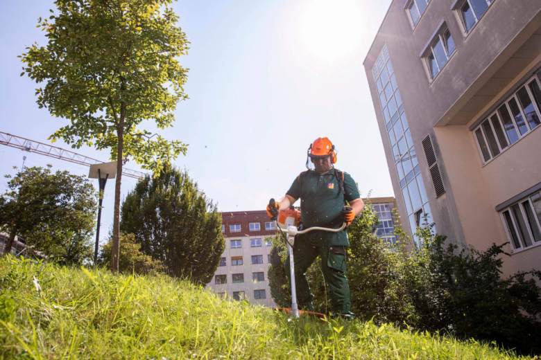 Mitarbeiter in Schutzkleidung und Helm bedient einen Freischneider zur Rasenpflege.