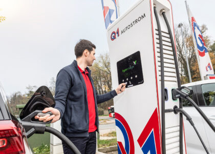 Mann lädt sein Elektroauto an einer Q1-Ladestation und bedient dabei mit einem Ladechip das Display der Schnellladesäule.