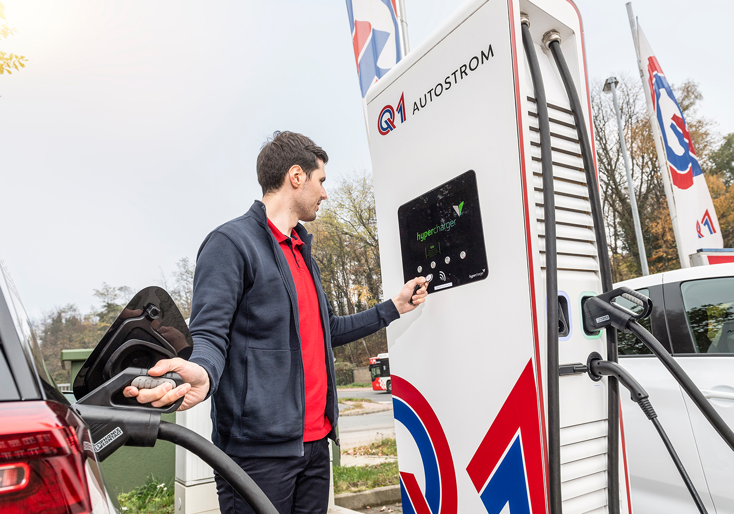 Mann lädt sein Elektroauto an einer Q1-Ladestation und bedient dabei mit einem Ladechip das Display der Schnellladesäule.