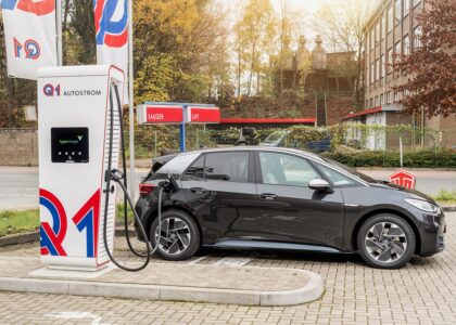 Dunkelgraues Elektroauto lädt an einer weißen Q1-Schnellladesäule auf einem Tankstellengelände.