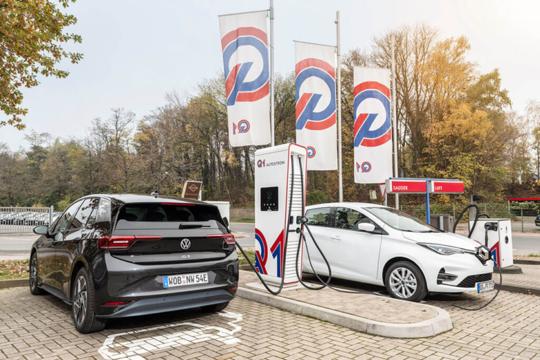 Zwei Elektroautos laden an einer Q1-Ladesäule unter wehenden Firmenfahnen.