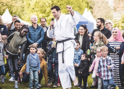 Sebastian Häfker im weißen Judo-Anzug spricht mit einem Mikrofon in der Hand vor einer großen, klatschenden Menschenmenge im Freien.