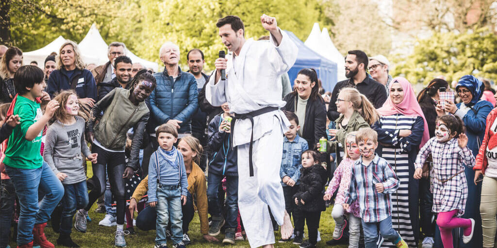 Sebastian Häfker im weißen Judo-Anzug spricht mit einem Mikrofon in der Hand vor einer großen, klatschenden Menschenmenge im Freien.