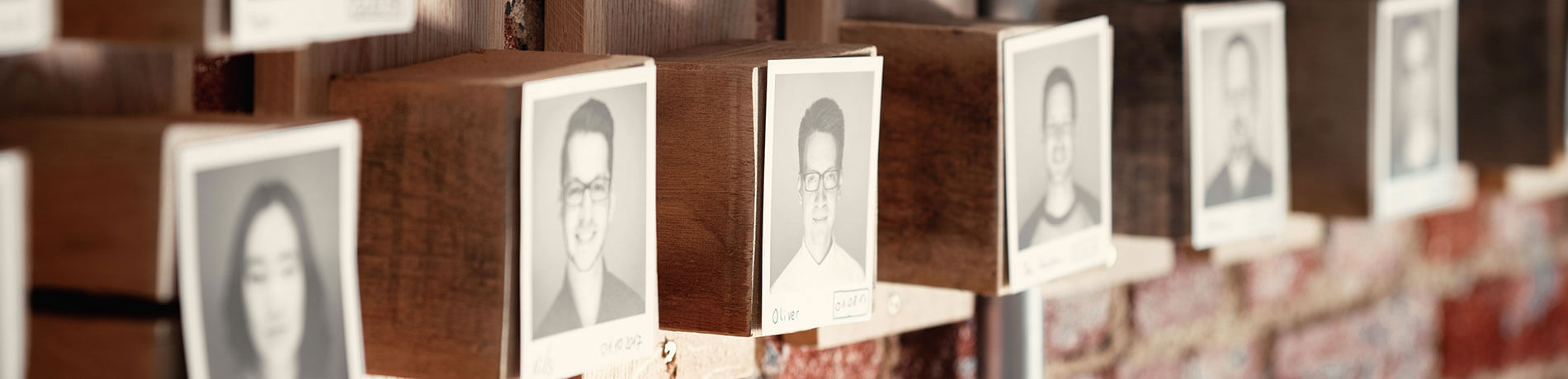 Schwarz-Weiß-Porträts von Teammitgliedern auf Holzblöcken vor einer Backsteinwand.