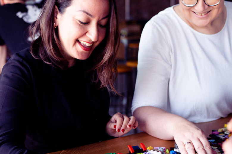 Zwei Frauen sitzen an einem Tisch und sortieren bunte Lego-Steine.