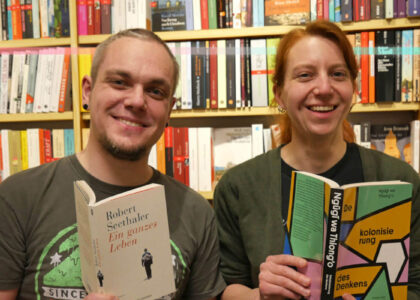Kathrin Bruhn und Bastian Lenzen vor einem Bücherregal mit jeweils einem Buch in der Hand