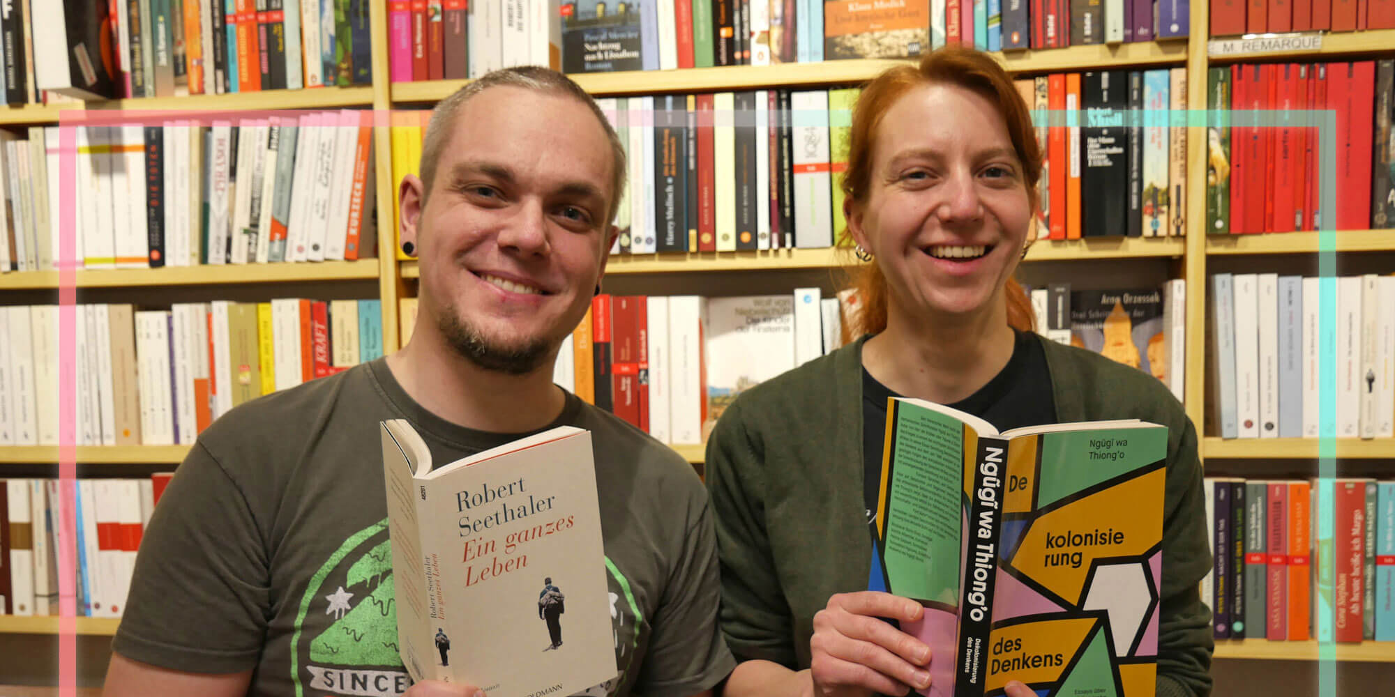 Kathrin Bruhn und Bastian Lenzen vor einem Bücherregal mit jeweils einem Buch in der Hand
