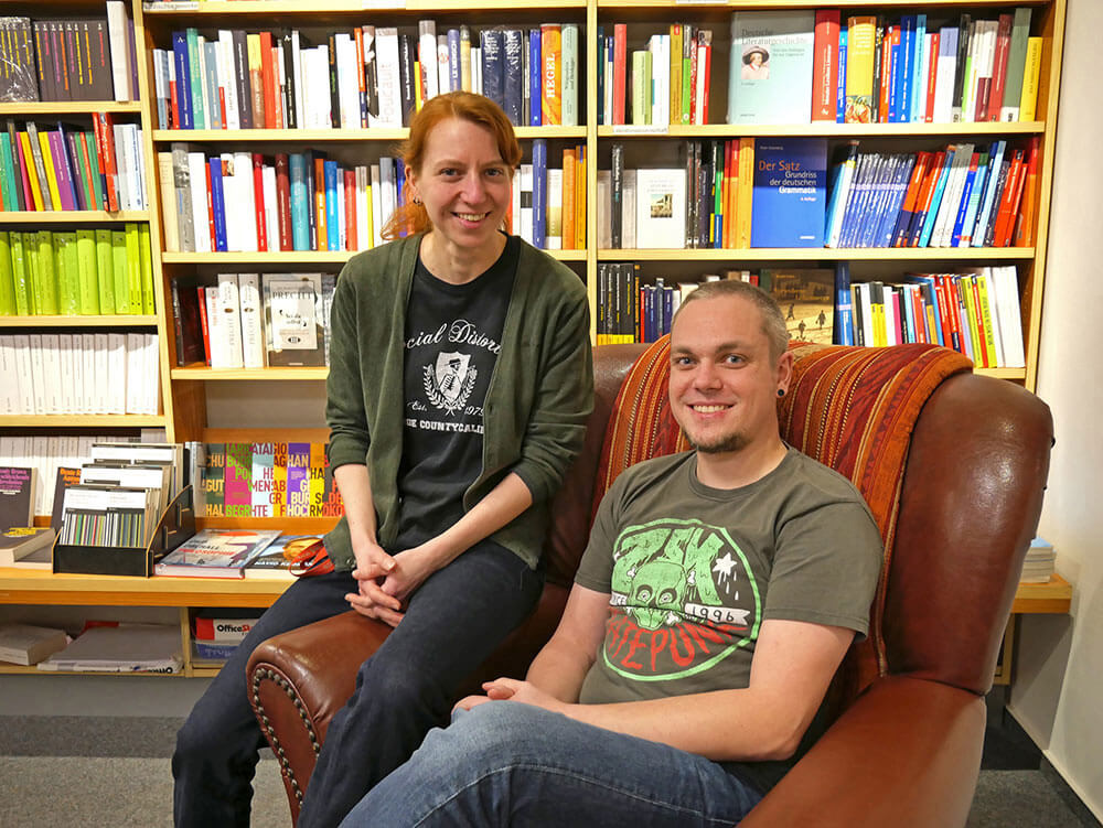 Kathrin Bruhn und Bastian Lenzen vor einem Bücherregal sitzen in einem Sessel