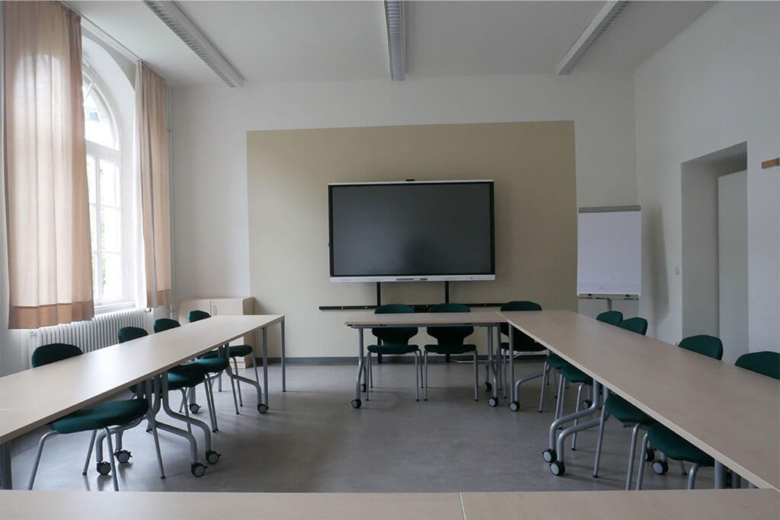 Heller Seminarraum mit hufeisenförmig angeordneten Tischen, Stühlen und einem digitalen Smartboard.