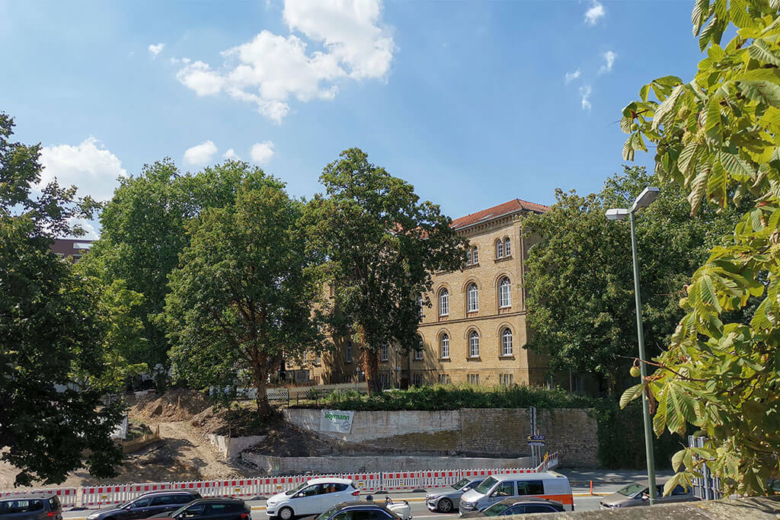Historisches Sandsteingebäude der VHS Osnabrück hinter Bäumen von einer Straße aus gesehen.
