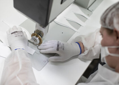 Person in Schutzkleidung verarbeitet weiße Atemschutzmasken präzise an einer speziellen Industriemaschine.