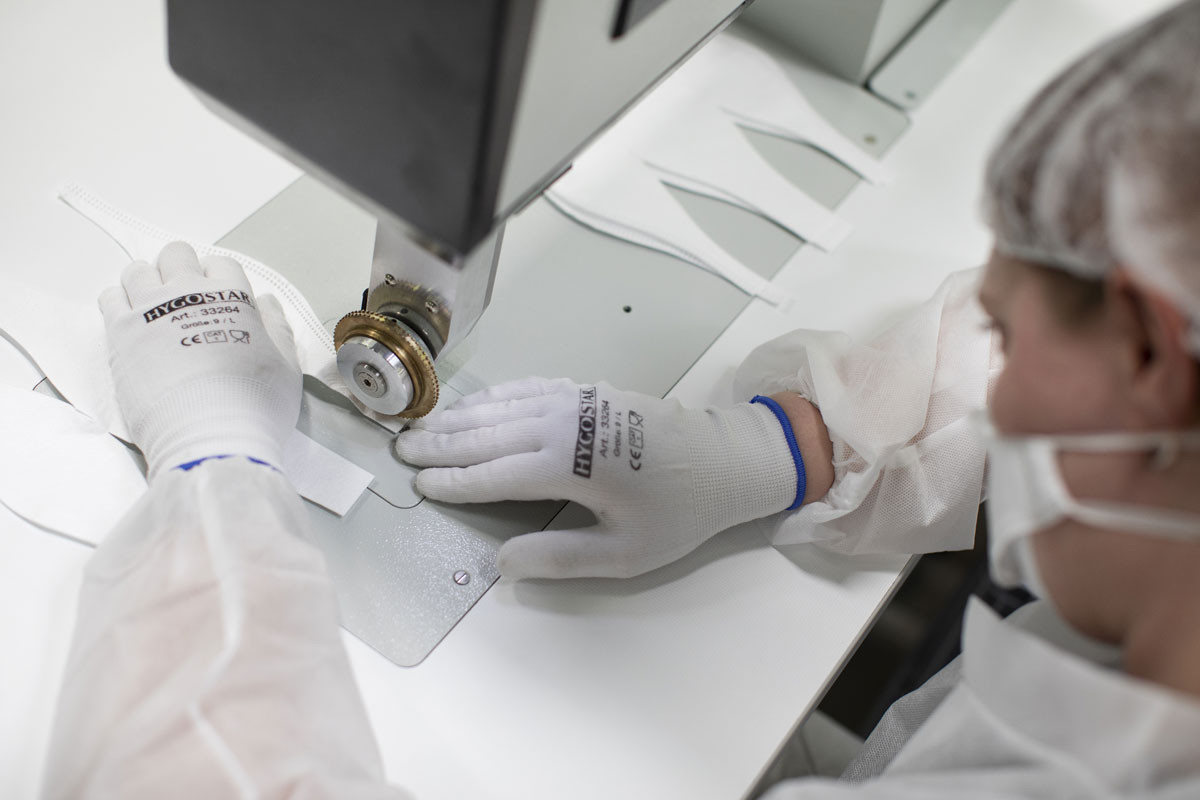 Person in Schutzkleidung verarbeitet weiße Atemschutzmasken präzise an einer speziellen Industriemaschine.