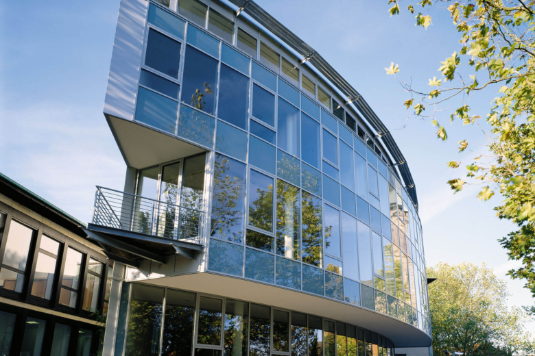 Moderne, geschwungene Glasfassade eines Bürogebäudes bei Sonnenschein und blauem Himmel.