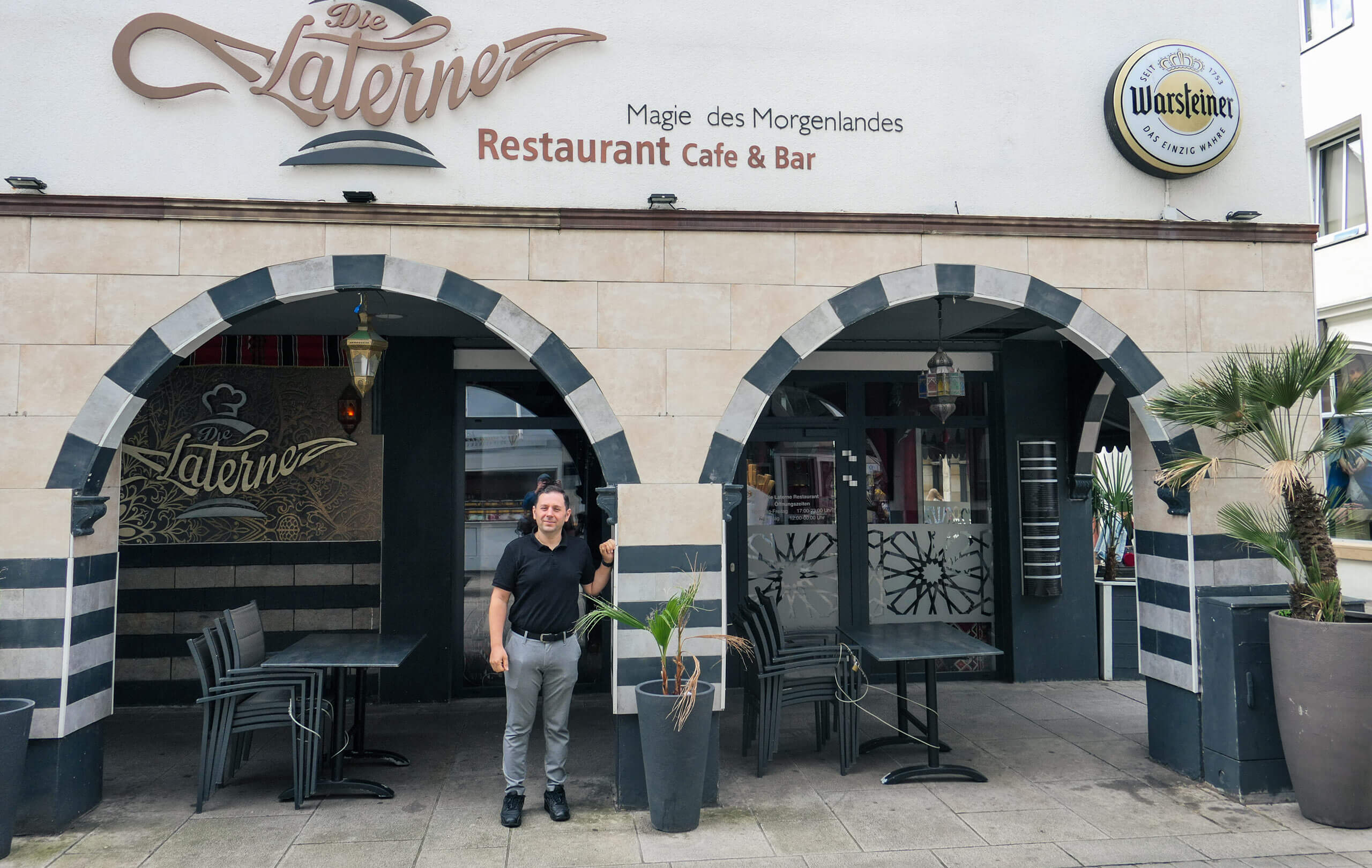 Ein Mann steht lächelnd vor dem Eingang des Restaurants Die Laterne unter orientalischen Bögen.