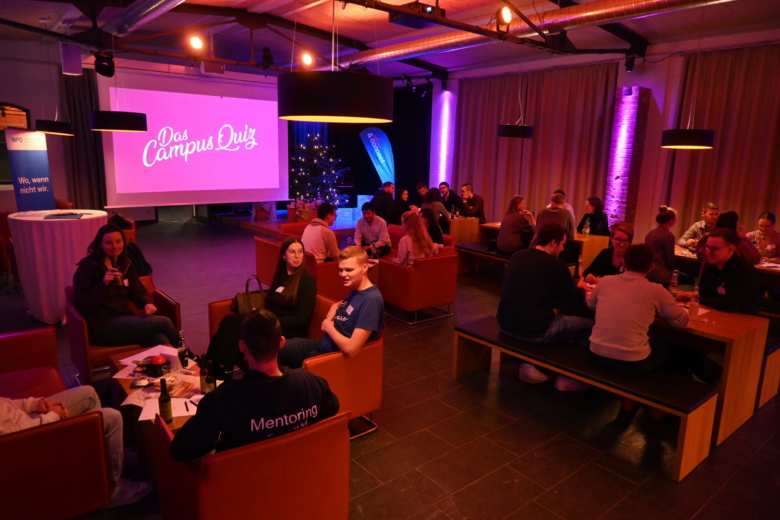 Quiz-Veranstaltung in stimmungsvoll beleuchteter Lounge mit mehreren Tischen, an denen Personen gemeinsam sitzen.