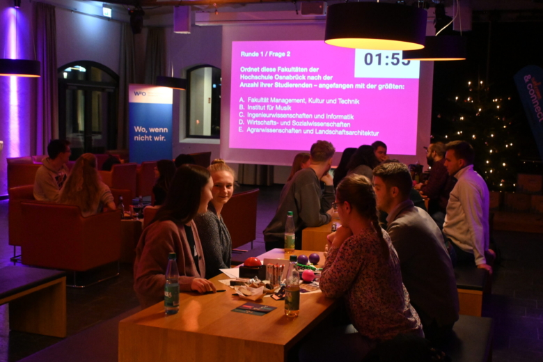 Studierende sitzen an Tischen vor einer Leinwand mit einer Multiple-Choice-Quizfrage zur Hochschule Osnabrück.