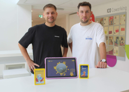 Zwei Männer stehen lächelnd hinter einem Tisch mit einem Tablet und gelben Lernkarten.