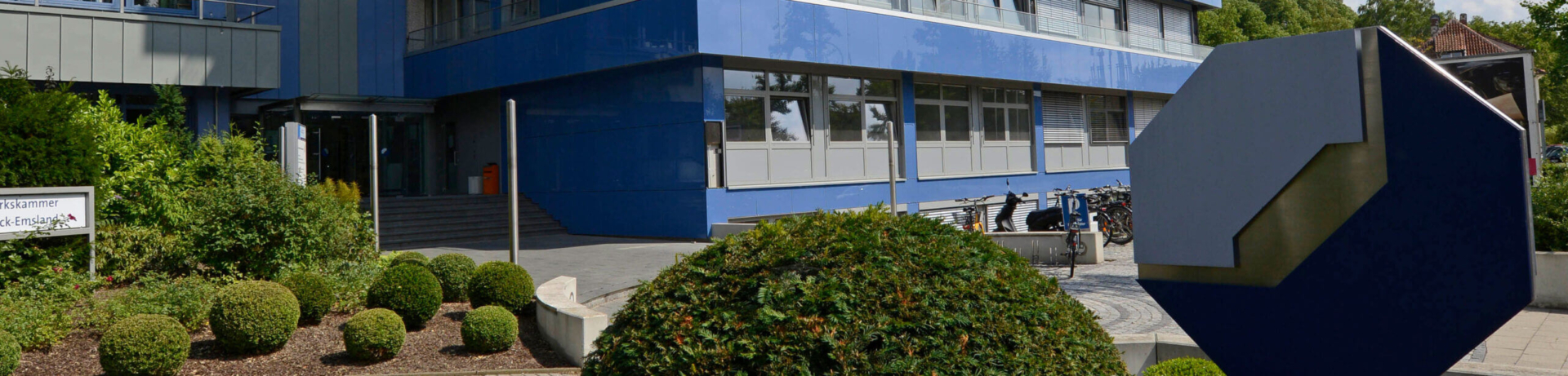 Modernes blaues Gebäude der Handwerkskammer Osnabrück mit gepflegten Buchsbäumen und blauem Logo im Vordergrund.