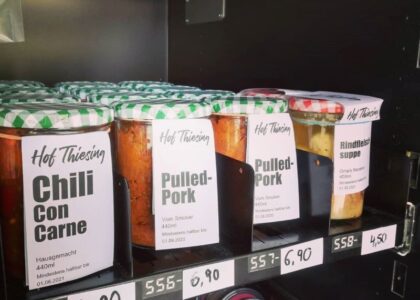 Konservengläser mit Gerichten wie Chili Con Carne vom Hof Thiesing stehen geordnet mit Preisschildern in einem Verkaufsregal.