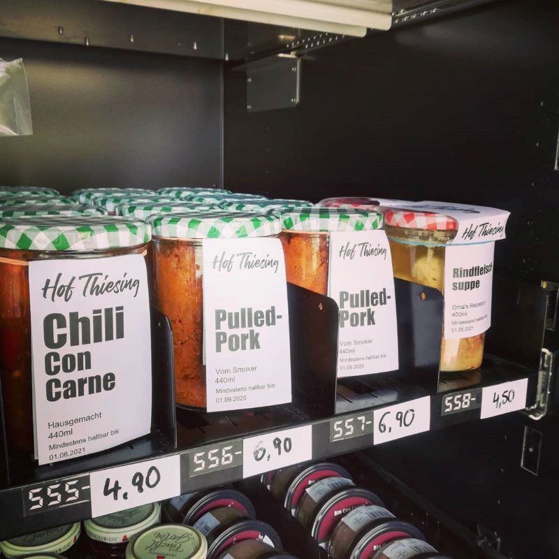 Konservengläser mit Gerichten wie Chili Con Carne vom Hof Thiesing stehen geordnet mit Preisschildern in einem Verkaufsregal.