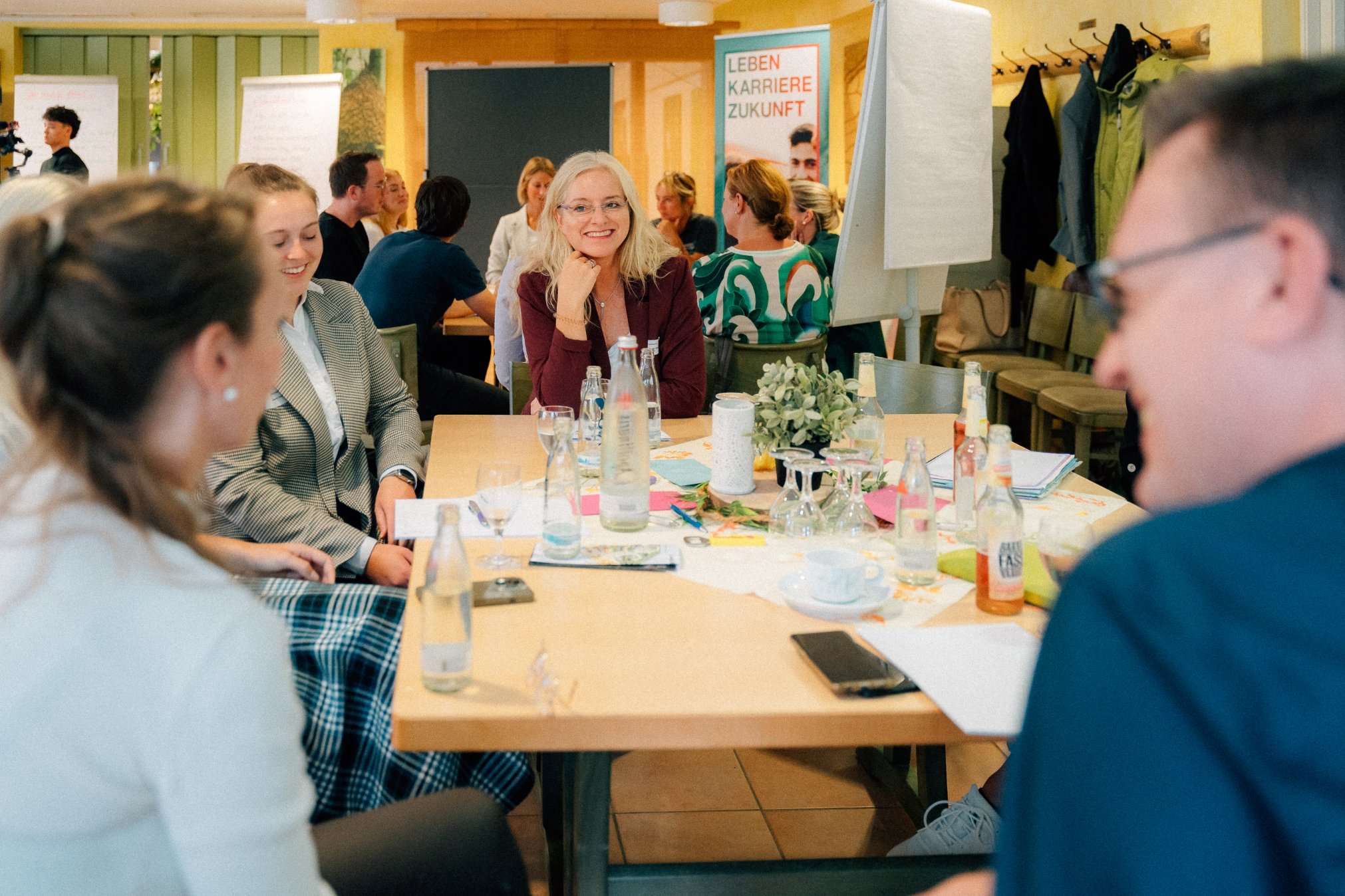 Lächelnde Menschen sitzen während eines Workshops im Gespräch an einem gedeckten Holztisch.