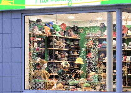 Schaufenster eines Hutgeschäfts mit dem Schriftzug Hutmanufaktur. Im Regal sind zahlreiche Hüte aufgereiht, unten steht: Hier werden Sie gut behütet.