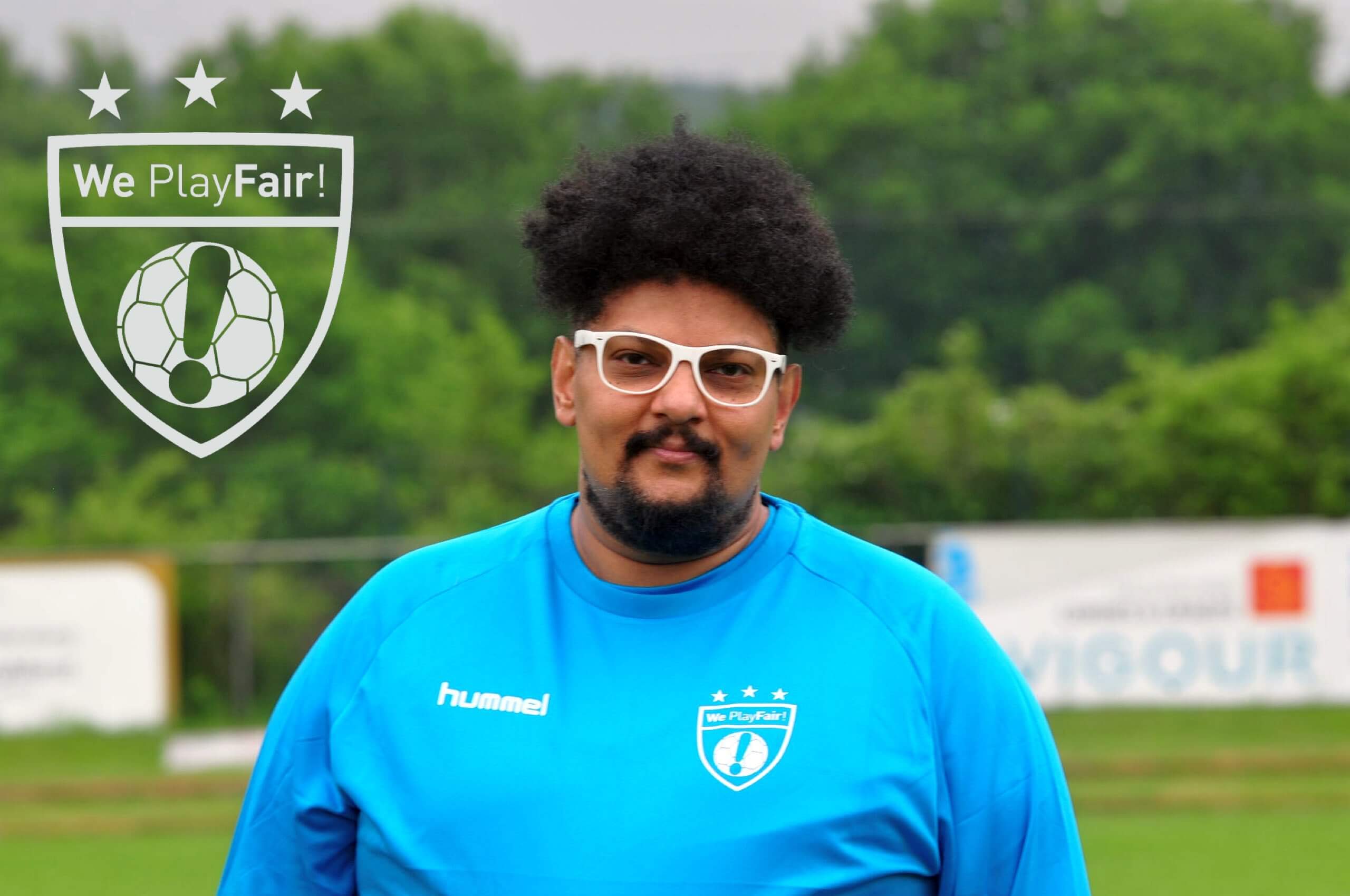 Kenny in blauem Trainingsshirt mit Brille vor grünem Hintergrund und We Play Fair!-Logo.