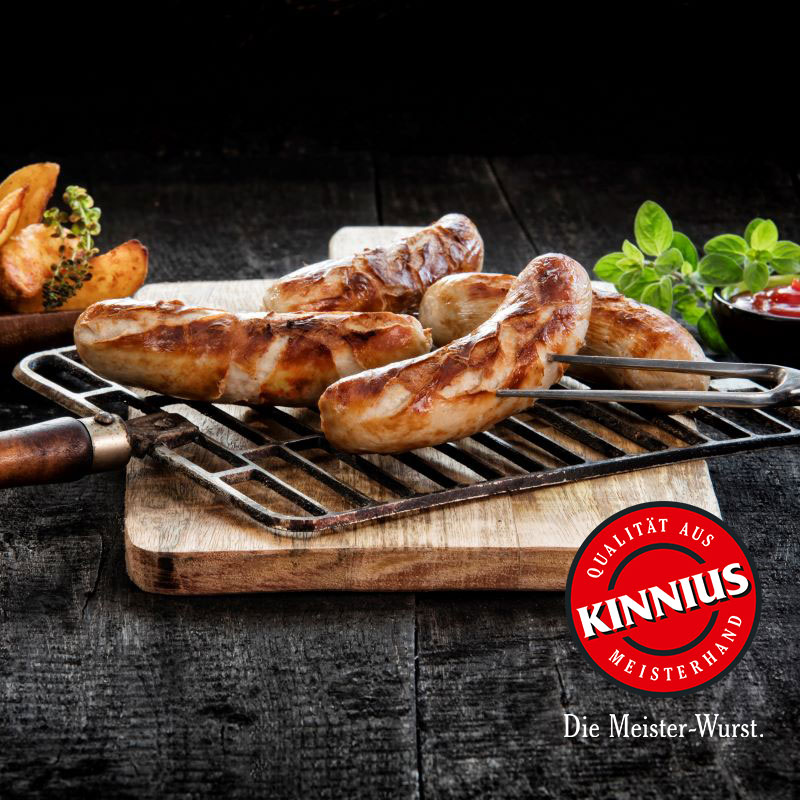Gegrillte Bratwürste auf einem Grillrost über Holzbrett, mit Logo KINNIUS – Qualität aus Meisterhand und Schriftzug: Die Meister-Wurst.
