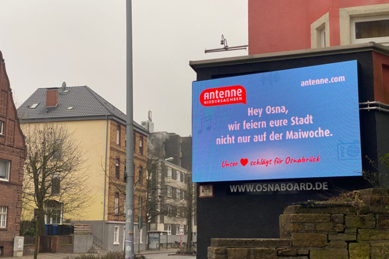 Ein beleuchtetes Display an einem Wohnhaus zeigt eine Grußbotschaft von Antenne Niedersachsen für die Stadt Osnabrück.