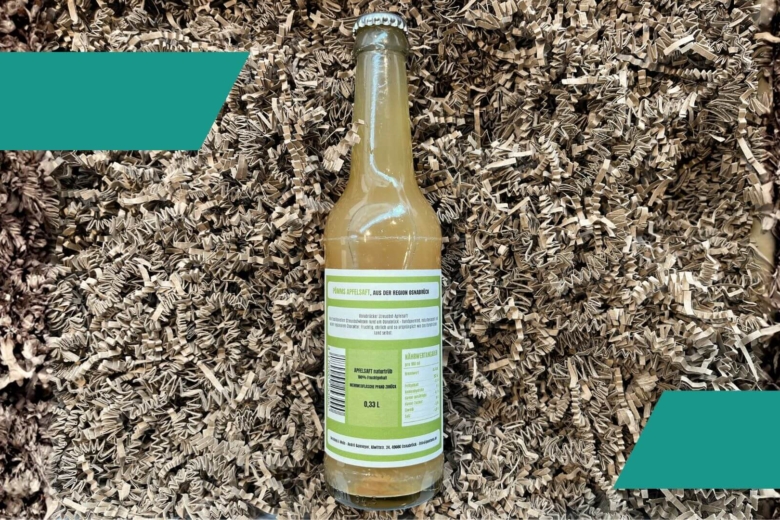 Glasflasche mit naturtrübem Apfelschaumwein von hinten mit Nährwerttabelle auf Papierschnipseln.