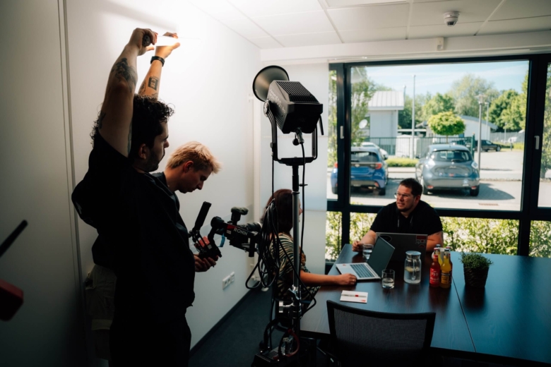 Videoteam richtet Kamera und Licht im Konferenzraum auf ein Gespräch am Tisch aus.