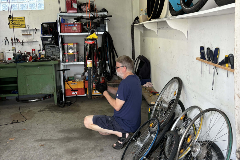 Ein Mann hockt in einer Garage und repariert die Kette eines aufgehängten Fahrrads.