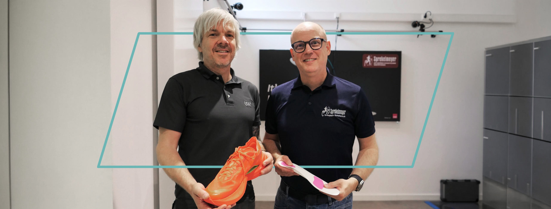 Zwei Männer präsentieren lächelnd einen orangefarbenen Laufschuh und eine Schuheinlage.