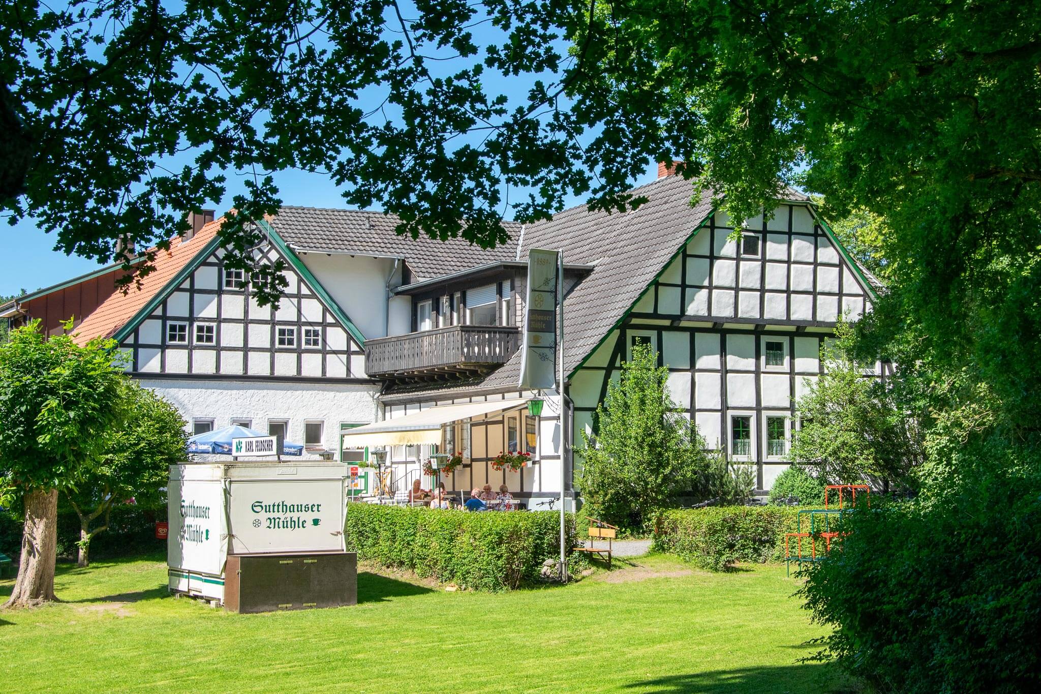 Fachwerkgutshaus mit Café-Ausschankwagen, Außengastronomie und gepflegter Rasenfläche bei Sonnenschein.