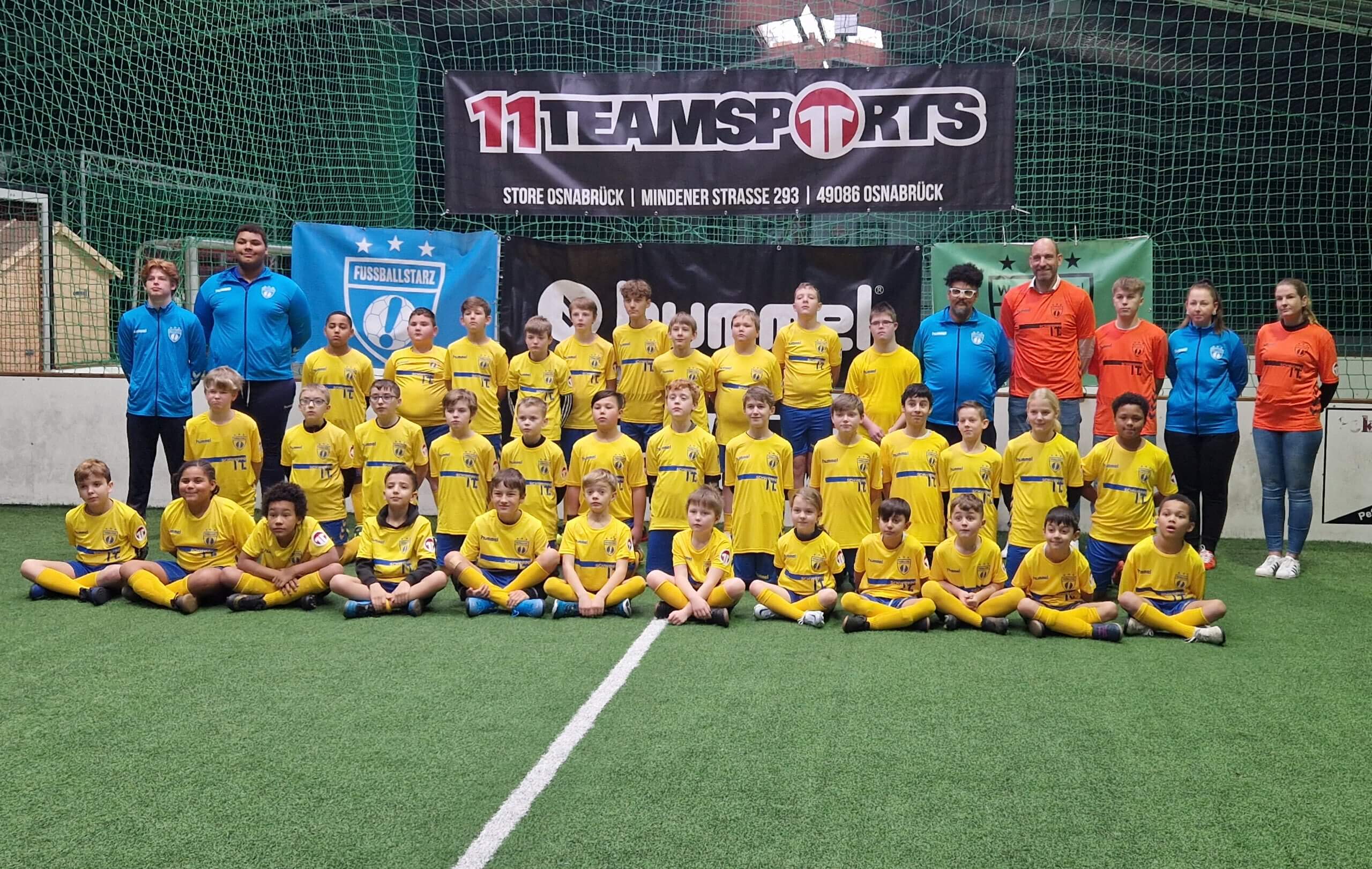 Große Kinder-Fußballmannschaft in gelben Trikots posiert mit ihren Trainern in einer Sporthalle.