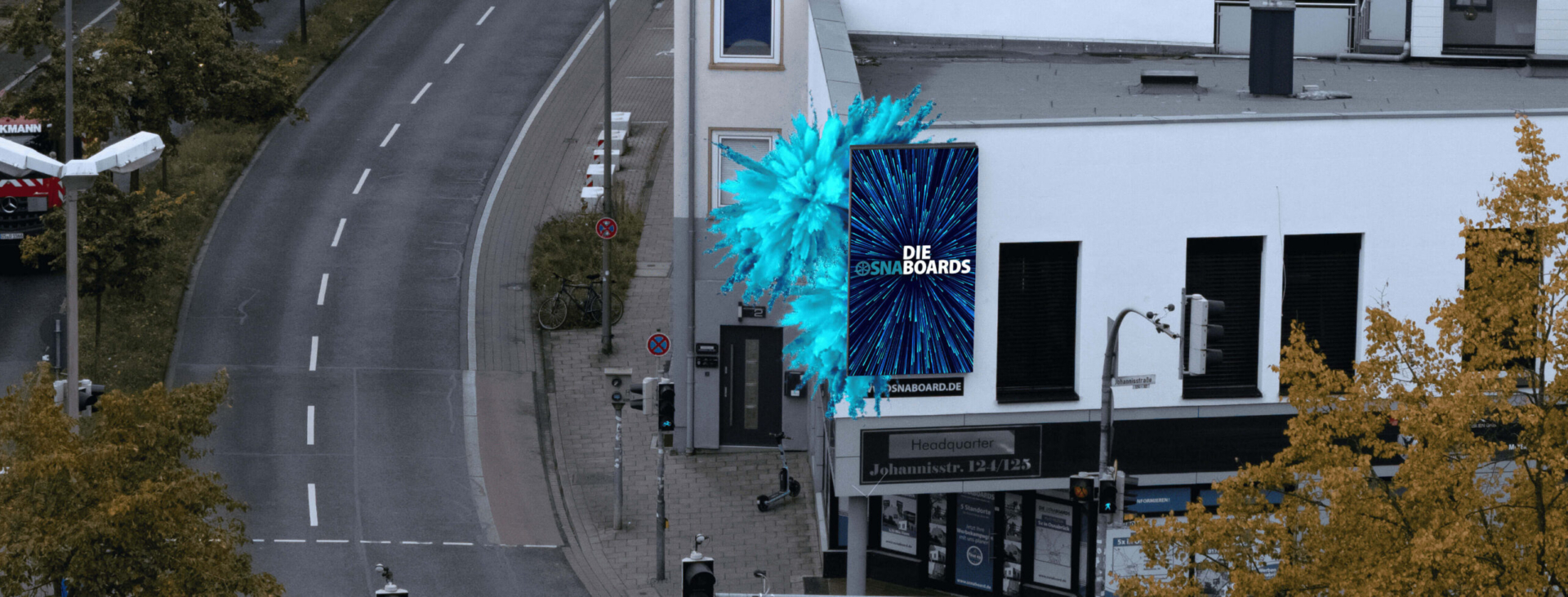 Draufsicht auf eine Kreuzung mit einem Gebäude, an dessen Ecke ein blaues digitales Werbeboard angebracht ist.